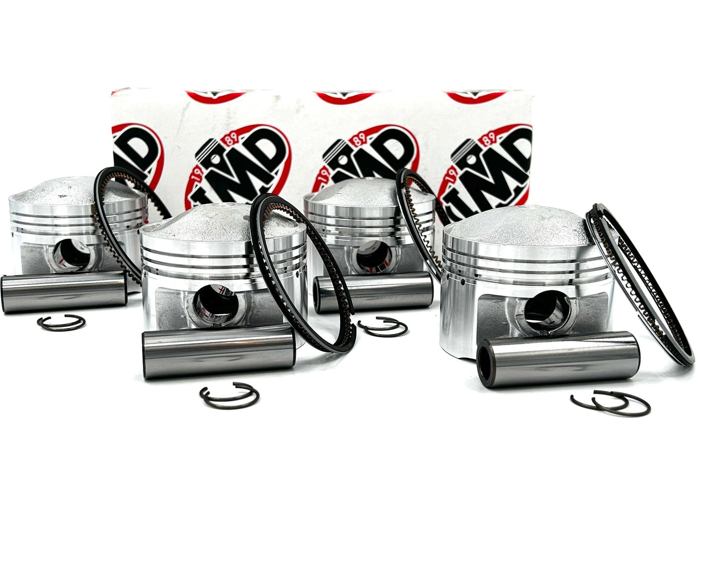 Four piston kits for a Suzuki GS1000 motorcycle, including pistons, rings, circlips, and pins, displayed against a white background.